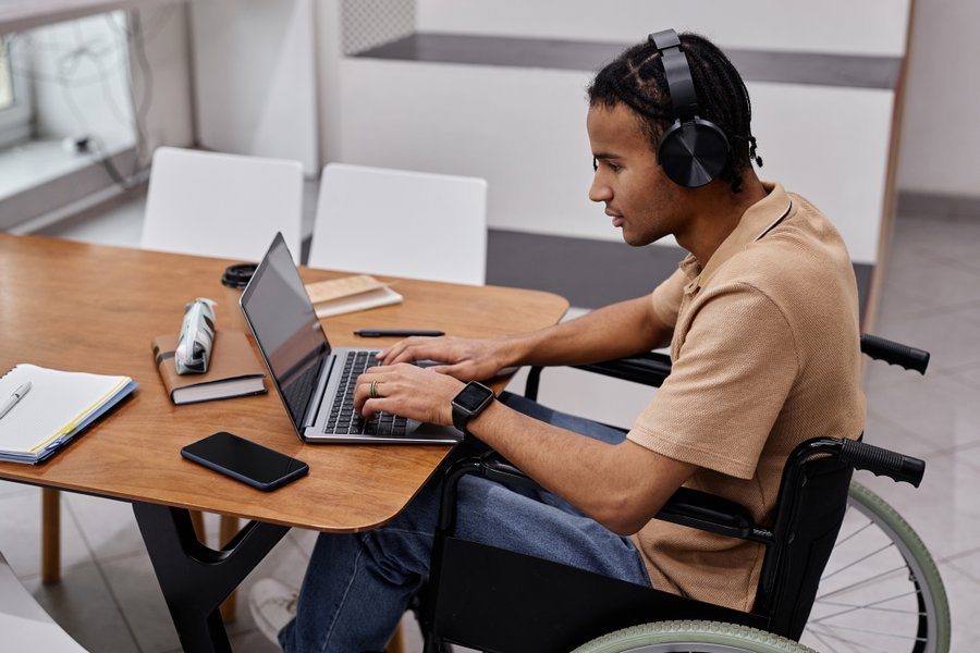 Student wearing headphones while working on a laptop computer, seated in a wheelchair