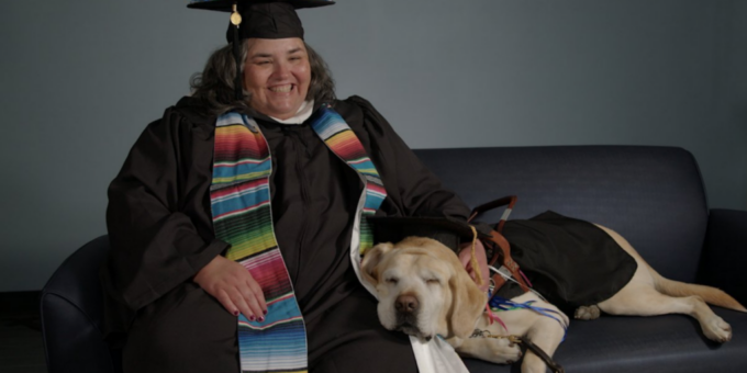 SNHU graduate smiling, seated on couch with service dog